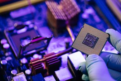 A gloved hand holds a computer processor chip above a motherboard, showing detailed circuitry and components in a close-up, high-tech setting.