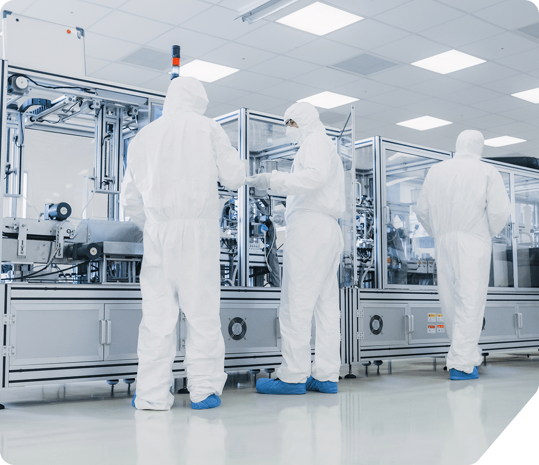semi-team Three people in full-body white protective suits and blue shoe covers work in a clean, modern laboratory or manufacturing facility with advanced equipment and bright overhead lighting.