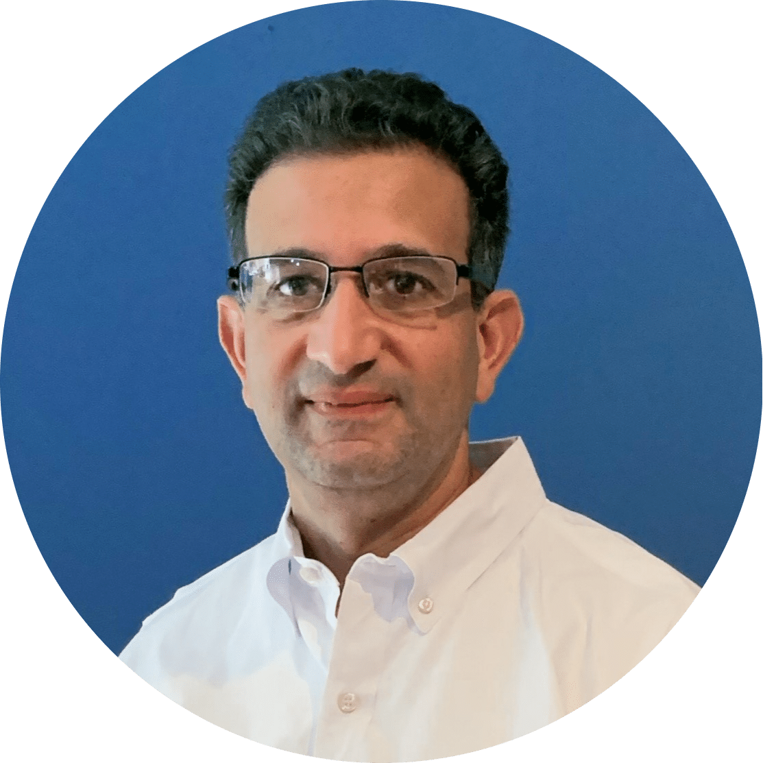 Aelan Mosden-modified A man with short dark hair, glasses, and a white button-down shirt smiles slightly in front of a solid blue background.