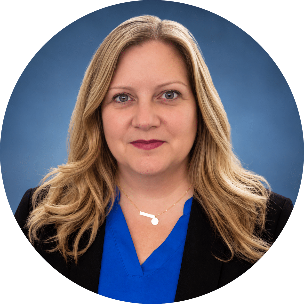Capri Woman with long blonde hair wearing a blue blouse and black blazer, looking at the camera with a neutral expression, photographed against a solid blue background.